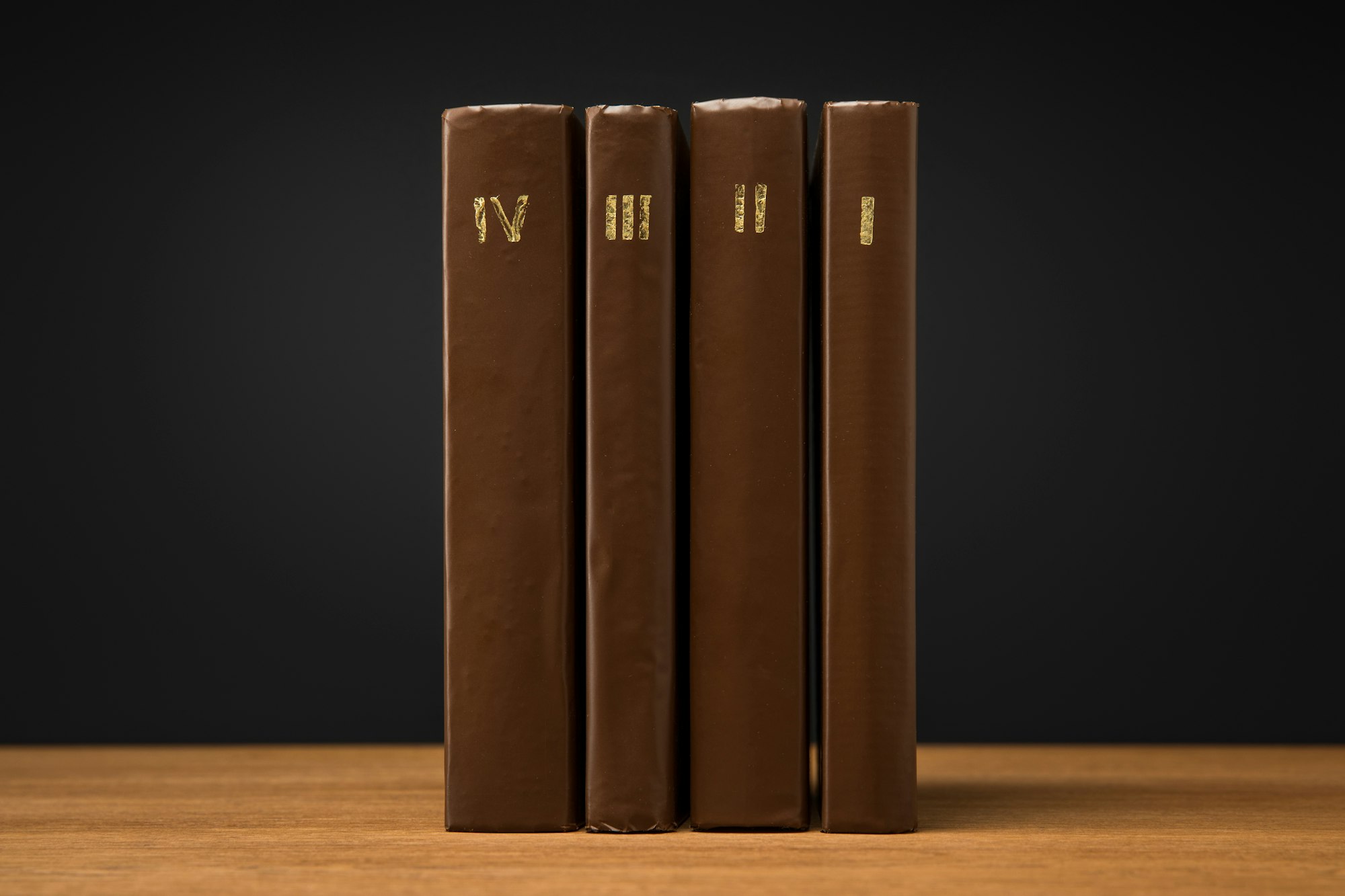 volumes of old books in leather brown covers on wooden table isolated on black