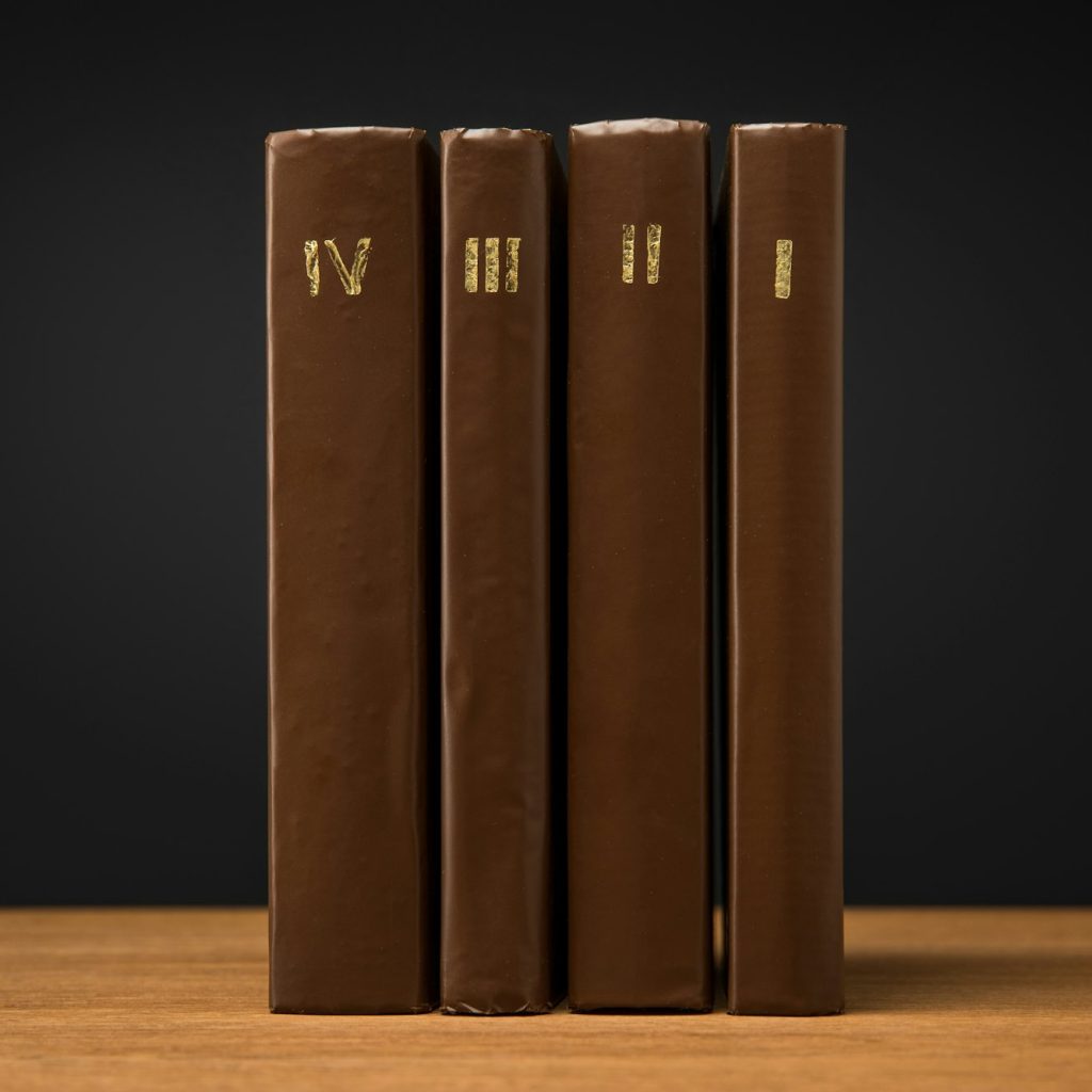 volumes of old books in leather brown covers on wooden table isolated on black